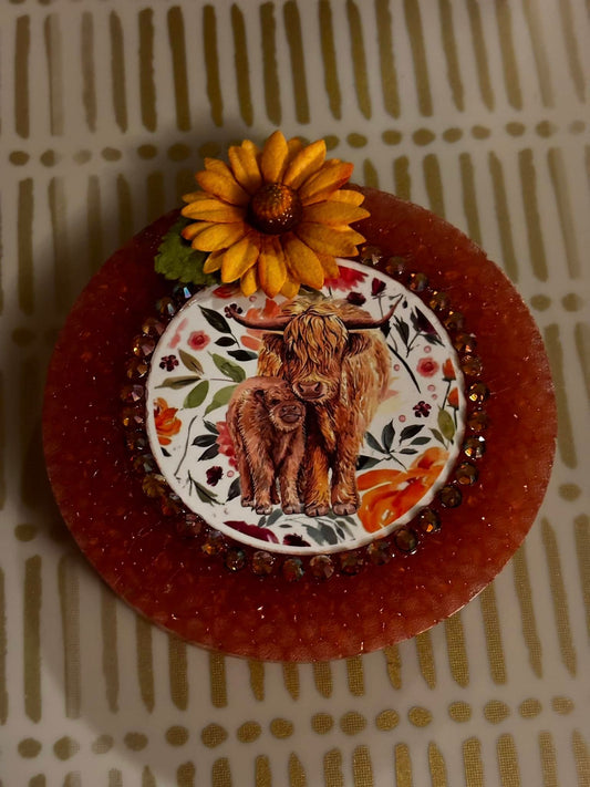 Round handmade car freshie with a Highland cow and calf image, floral background, gem border, and sunflower embellishment.