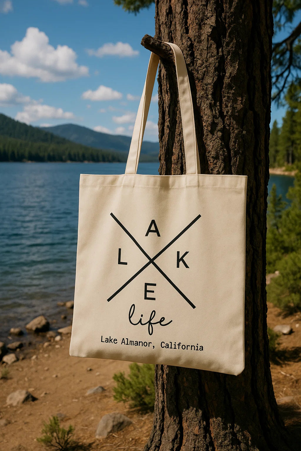 Natural canvas tote printed with “Lake Life” design and “Lake Almanor, California,” hanging on a tree by the lake.

