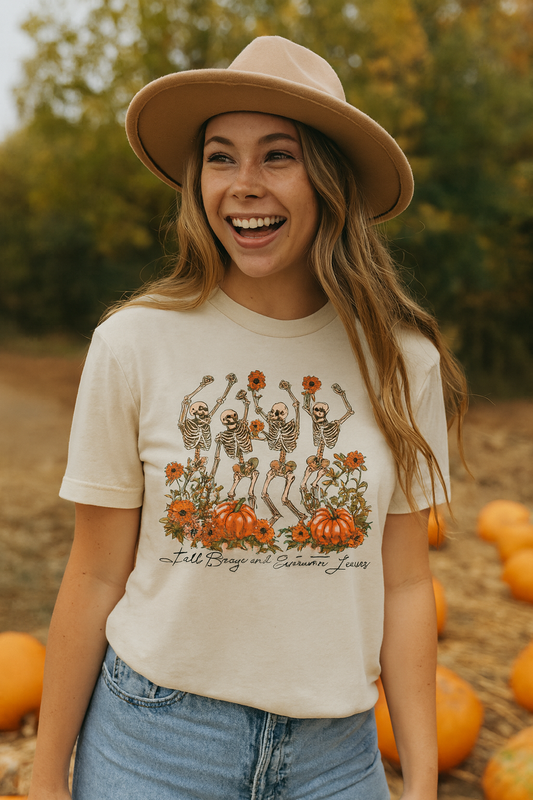 Soft cream Bella+Canvas 3001C t-shirt featuring a vintage-style design of dancing skeletons holding orange flowers, surrounded by pumpkins and autumn blooms, with the words "Fall Breeze and Autumn Leaves" in script.